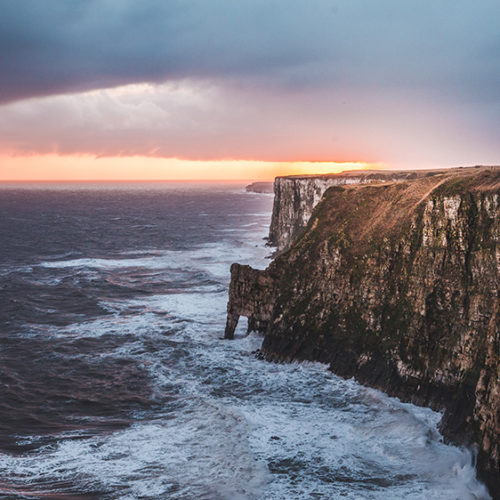 Ocean waves against cliff, cloudy skies and sunset